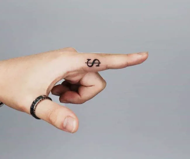 A dollar sign tattoo on the inside of finger